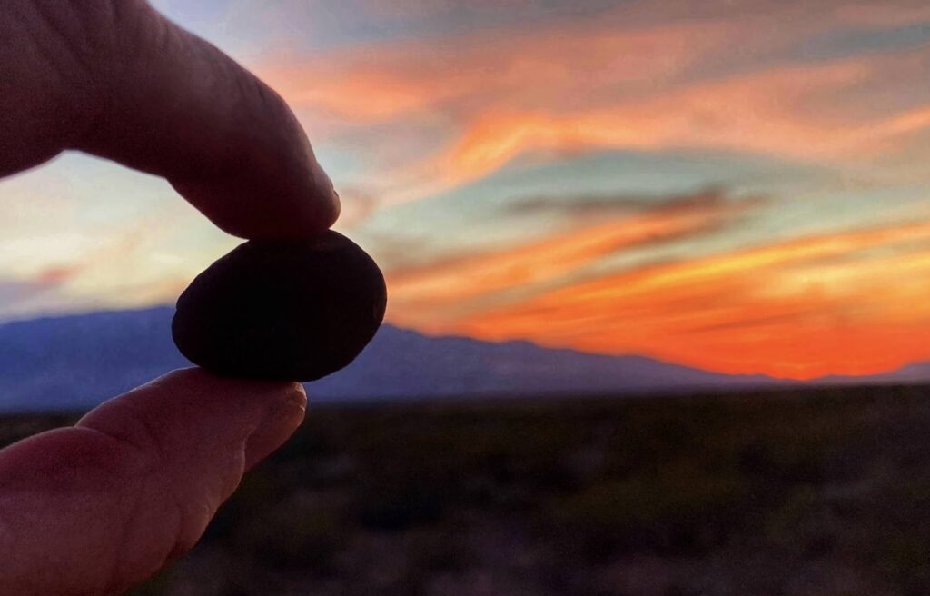A hand holding a large Saffordite stone while the sun sets over Mt. Graham near Safford, Arizona.