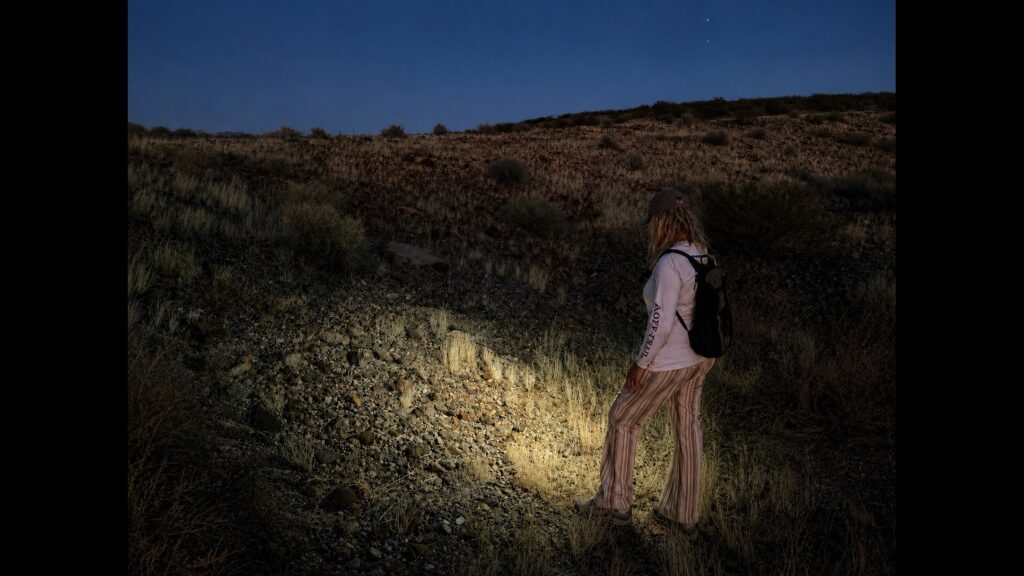 A person shining a strong flashlight on the desert ground at night searching for Saffordite stones.